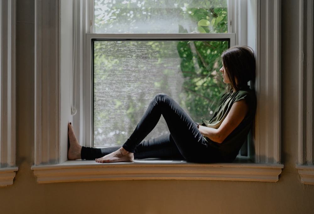 A woman sitting quietly on a window sill, deep in thought