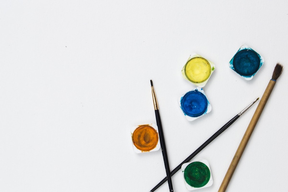 An assortment of colorful paints and paintbrushes used in expressive arts therapy