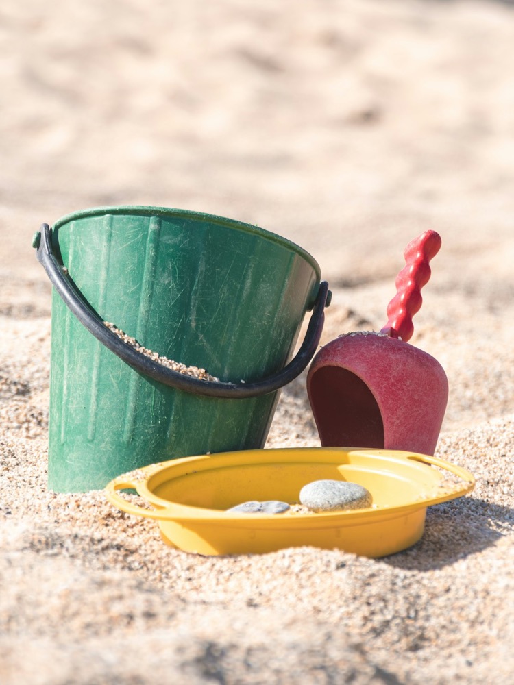 A sand tray with a bucket, scoop, and stones used in sand tray therapy