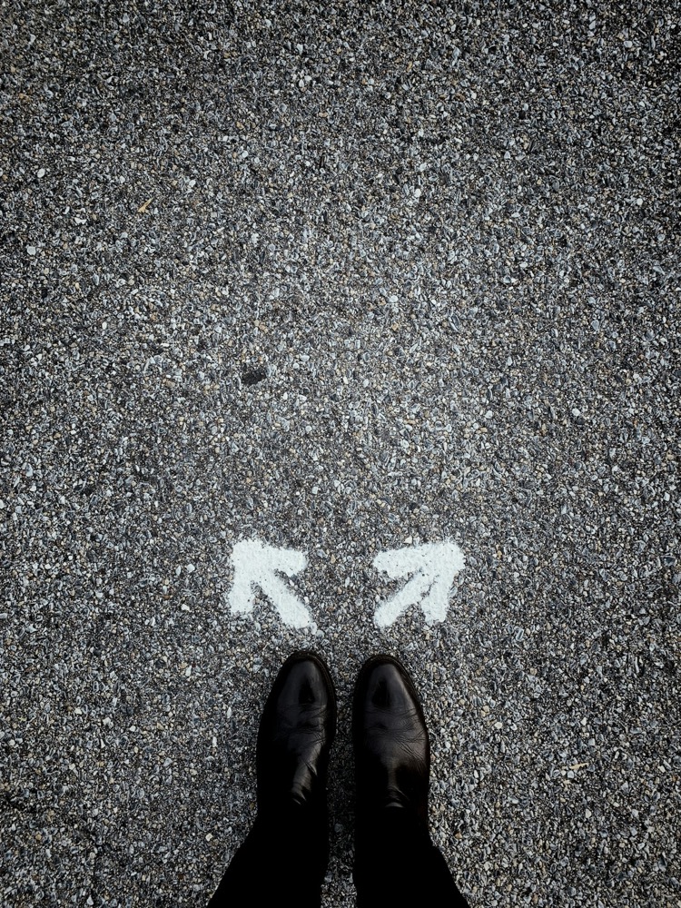 A person standing at a fork in the road marked by two painted arrows