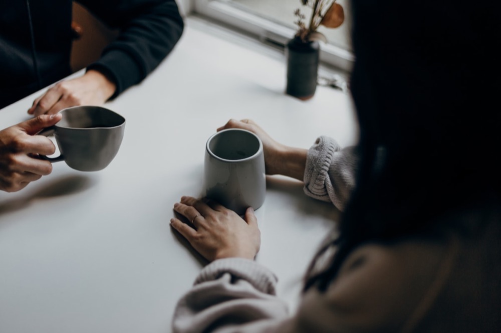 Two people in conversation, each holding a warm mug during a mentoring meeting
