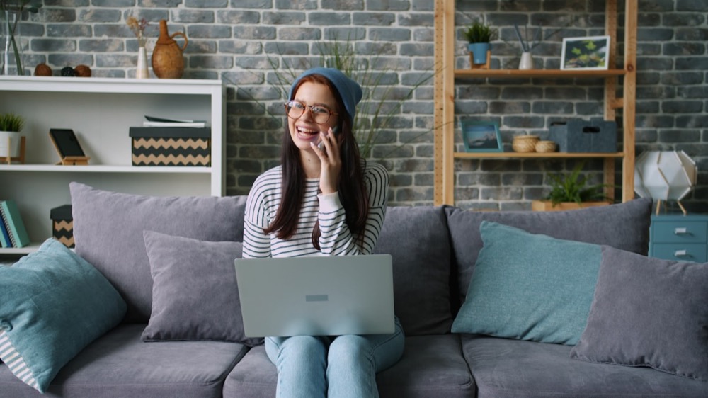 A woman talking on the phone with a laptop nearby on the couch