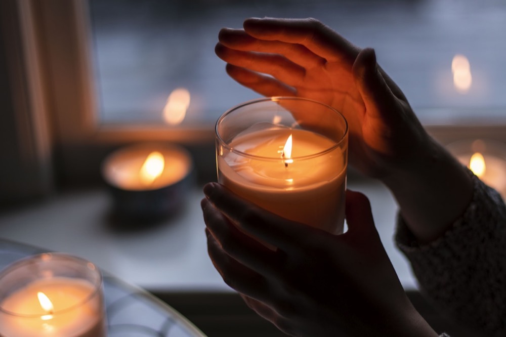 Hands cupped gently around a warm candle in soft light